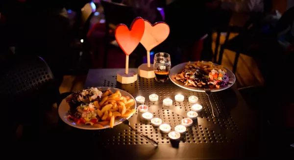 Stół w restauracji z dwiema potrawami, świecami, szklanką napoju i dekoracją w kształcie serc.